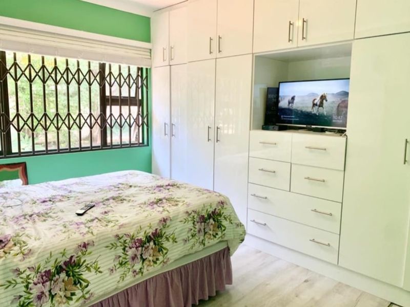 A bedroom featuring extensive white built-in cabinetry, laminate flooring, and a window fitted with a security gate.