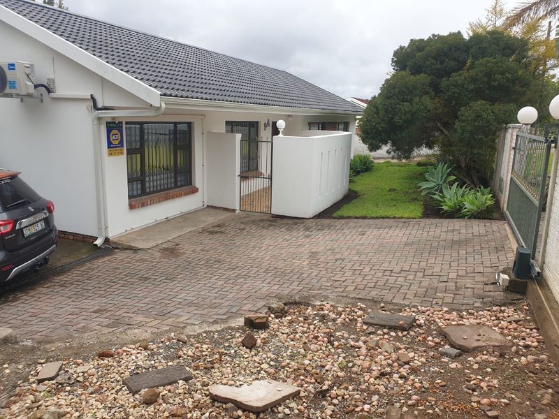 Front exterior view of a residential property featuring a paved driveway, security gate, and tiled roof with an installed air conditioning unit.