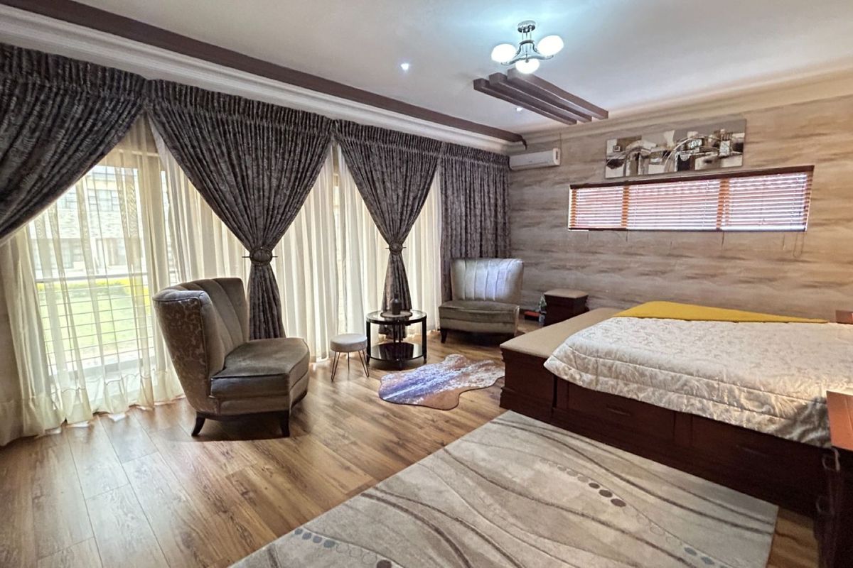Spacious bedroom featuring wood-look flooring, decorative ceiling detailing, wall-mounted air conditioning unit, and large sliding glass doors with integrated curtain tracks.
