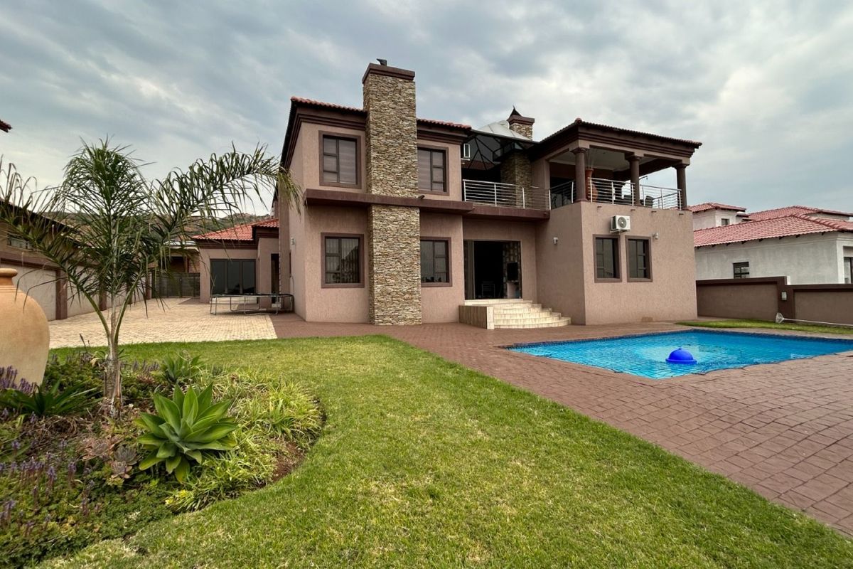 Rear view of a two-story house featuring a swimming pool, paved patio area, stone-clad chimney, and an upper-level balcony.