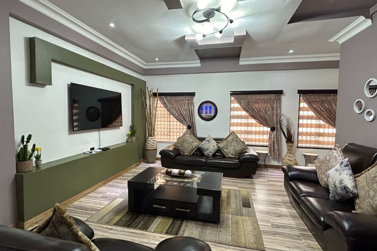Spacious living room featuring a custom built-in media wall, recessed ceiling details with integrated lighting, and modern wood-look flooring.