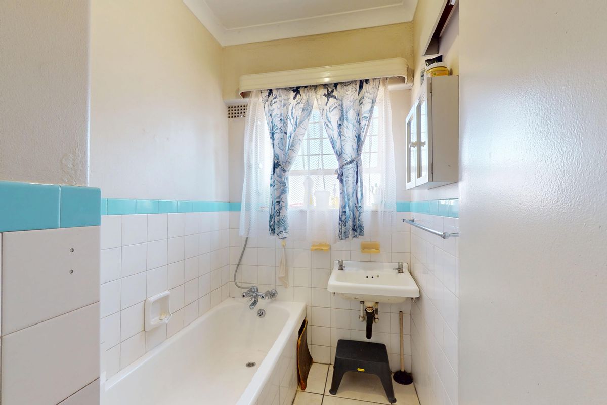 A compact bathroom featuring a built-in bathtub, wall-mounted basin, and classic white tiling with a decorative blue border.