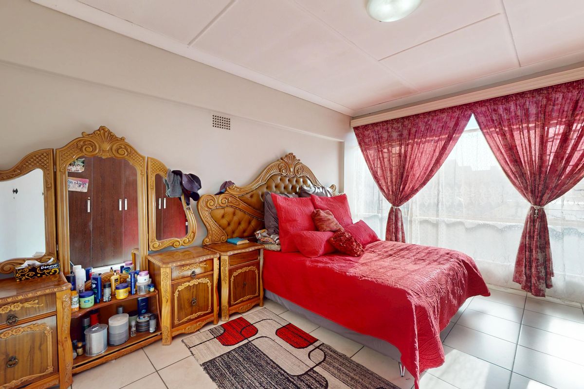 A spacious bedroom featuring tiled flooring, built-in cupboards, and large windows with natural light.