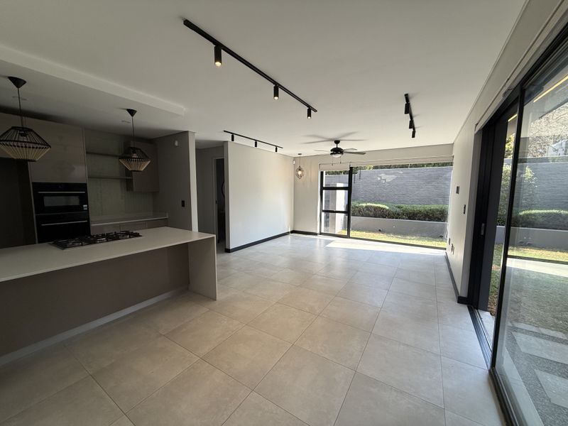 Modern open-plan living and kitchen area featuring a central island, built-in appliances, sleek track lighting, and large sliding doors opening to the garden.