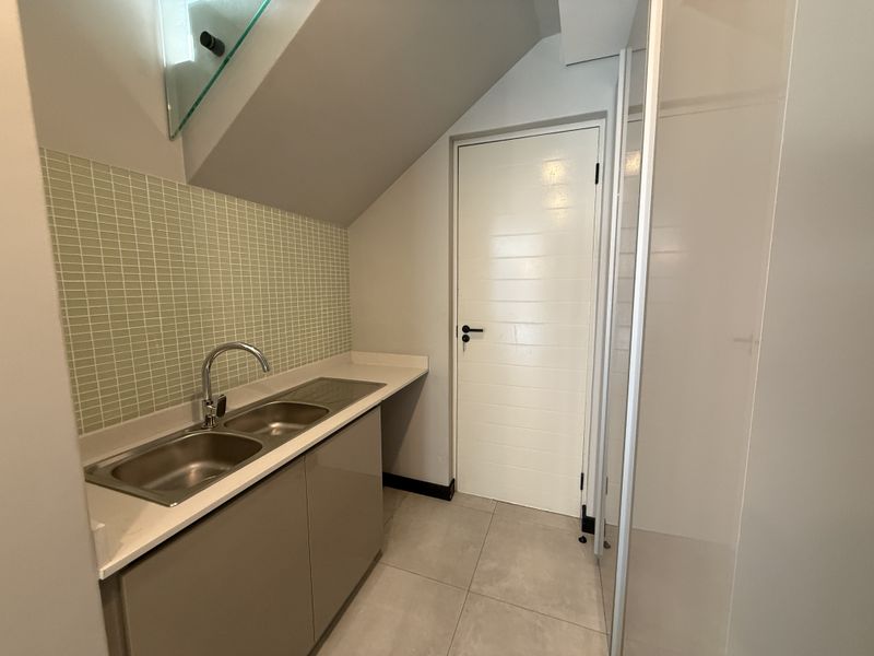A clean and functional scullery area featuring a double stainless steel sink, stone countertops, mosaic tile backsplash, and ample built-in cabinetry.