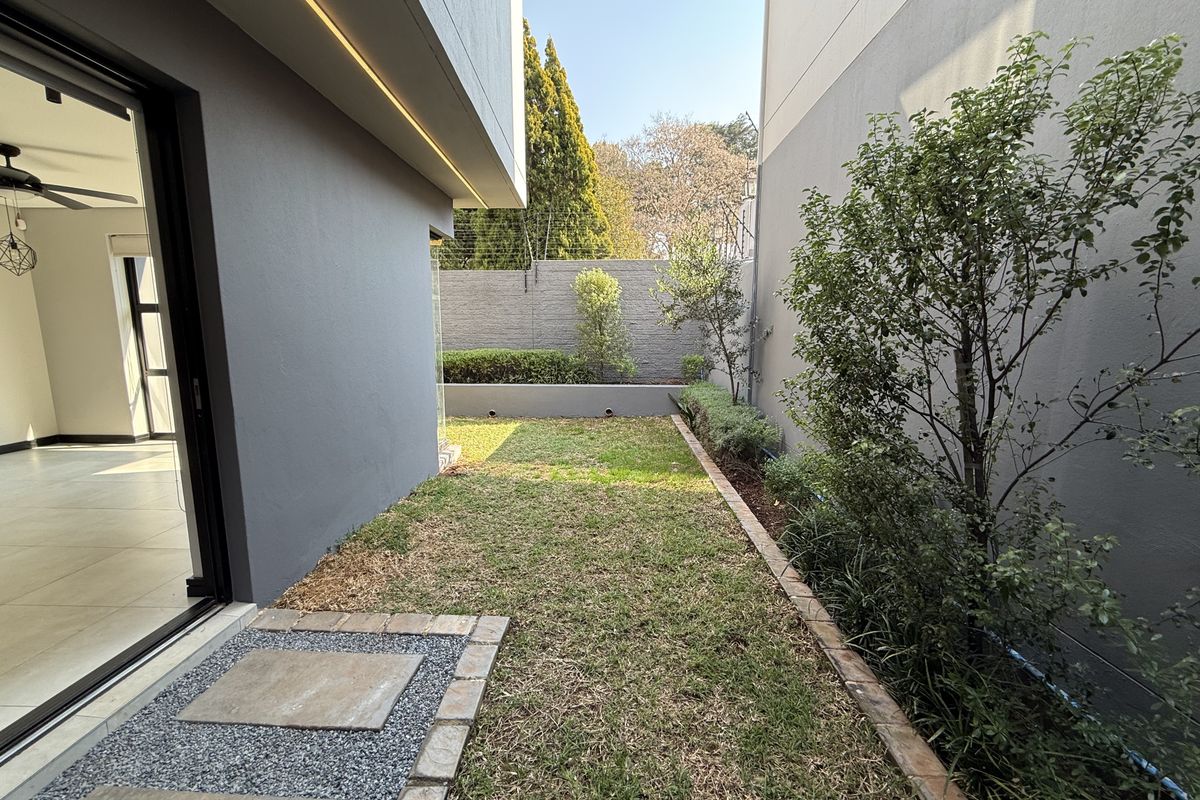 A private rear garden area featuring a manicured lawn, paved pathway, and secure boundary walls with electric fencing, accessible from the main living space.