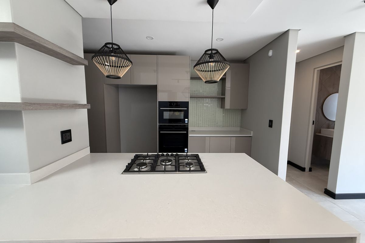 Modern kitchen featuring a central island with a gas hob, sleek gloss cabinetry, quartz countertops, and a stylish mosaic tile backsplash.