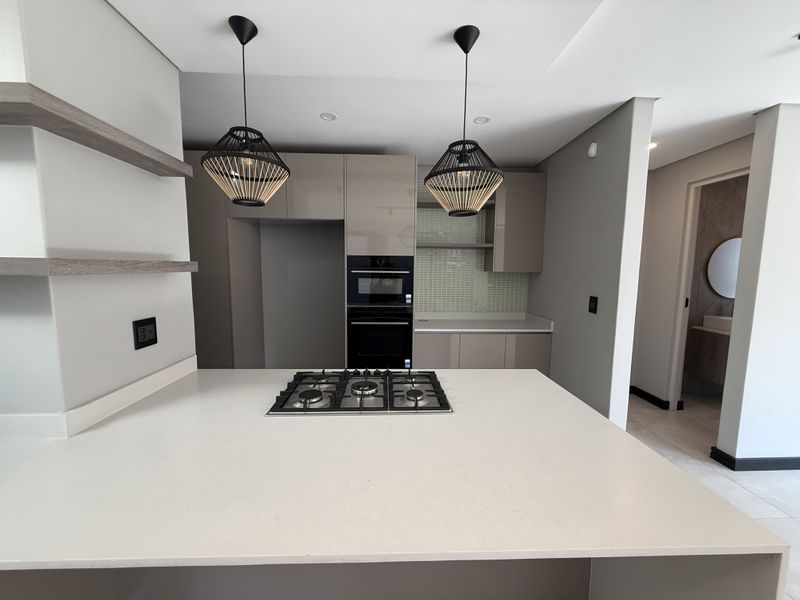 Modern kitchen featuring a central island with a gas hob, sleek gloss cabinetry, quartz countertops, and a stylish mosaic tile backsplash.