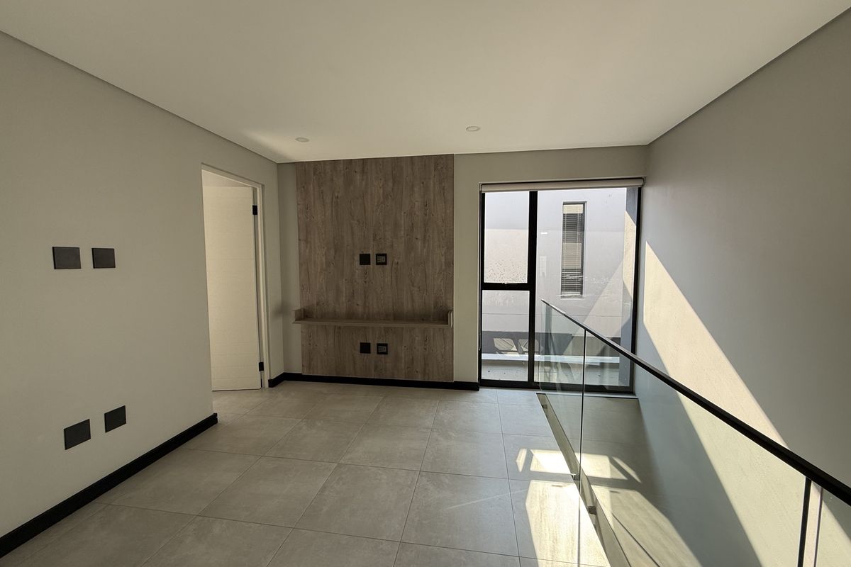 A bright, modern living area featuring large format floor tiles, a contemporary wood-look media feature wall, and a sleek glass balustrade overlooking the lower level.