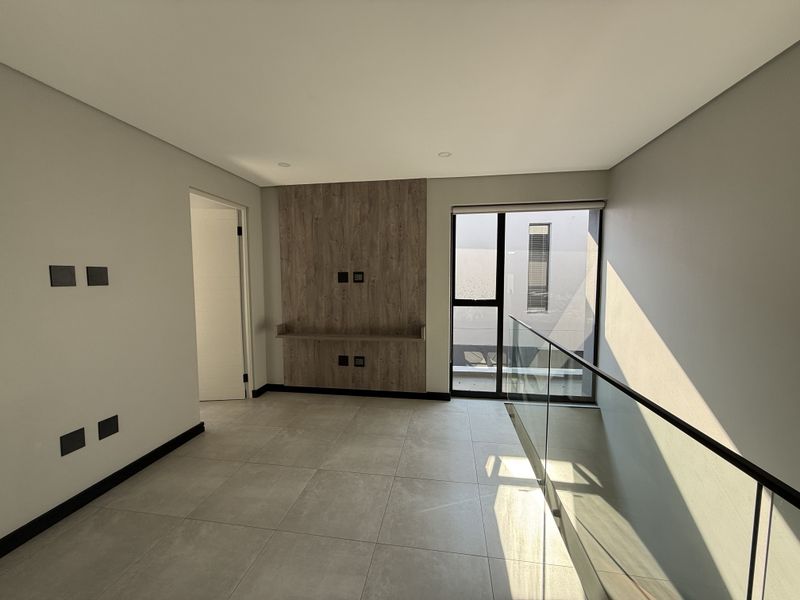 A bright, modern living area featuring large format floor tiles, a contemporary wood-look media feature wall, and a sleek glass balustrade overlooking the lower level.