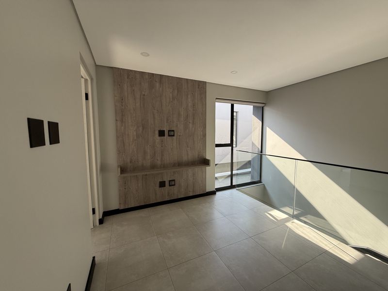 A modern, empty living area featuring a wood-look feature wall, tiled flooring, and a glass balustrade overlooking the staircase.