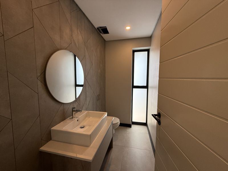 Modern bathroom featuring a vessel sink vanity, geometric tiled feature wall, and a frosted glass window providing natural light.