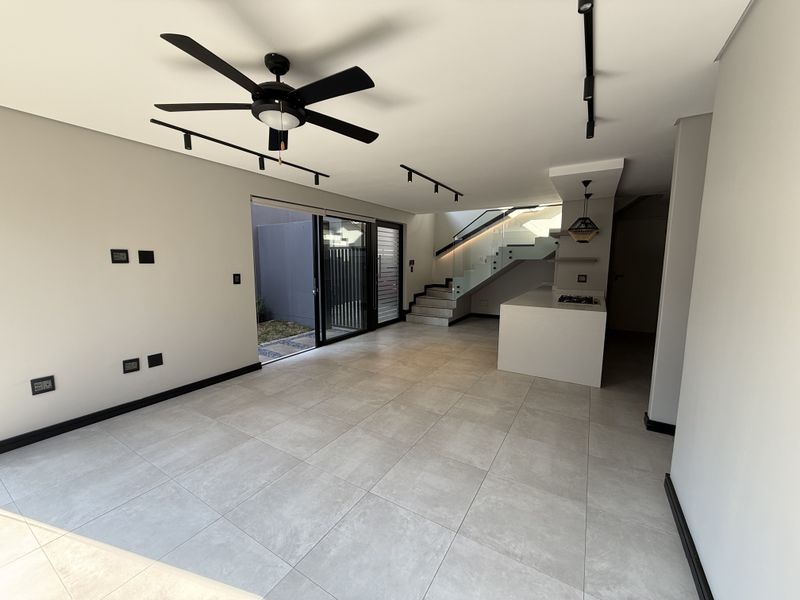 Spacious open-plan living area featuring modern tiled floors, track lighting, a sleek kitchen island with a gas hob, and a contemporary staircase.