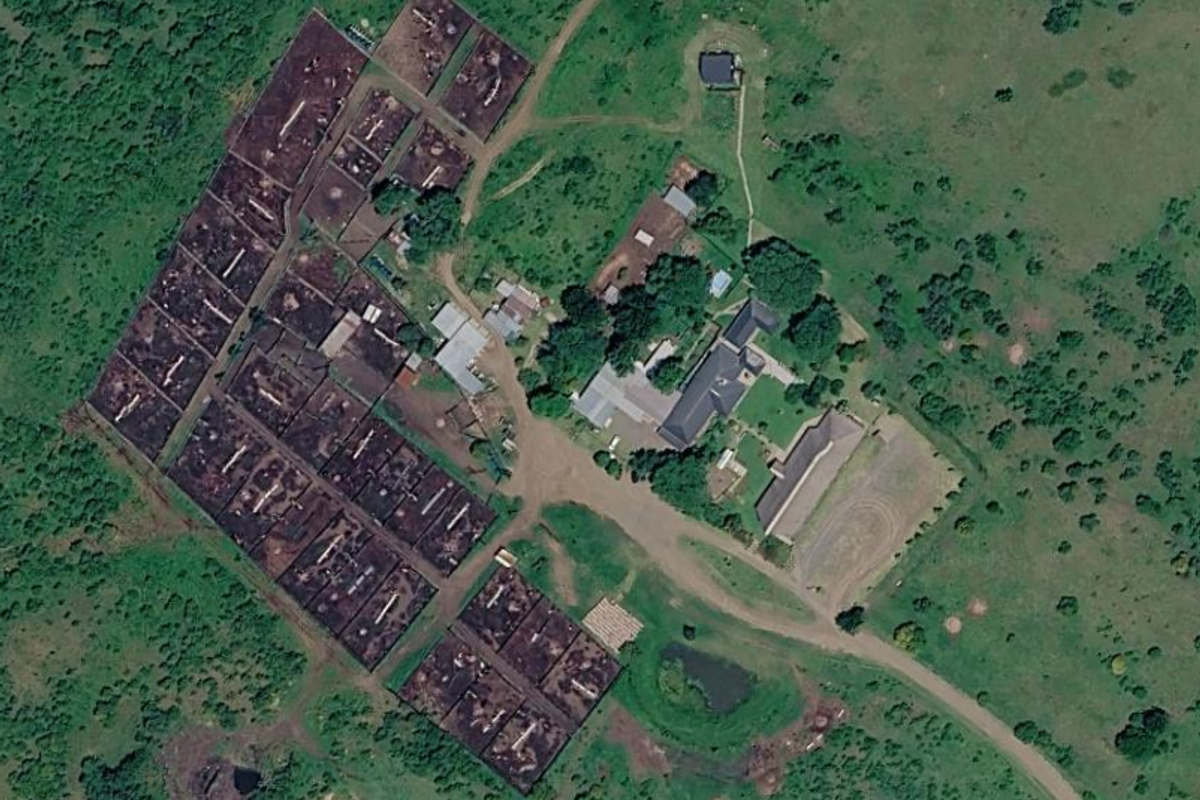 Aerial view of a farm property featuring a main residence, multiple outbuildings, livestock enclosures, and a small dam set within rural landscape.