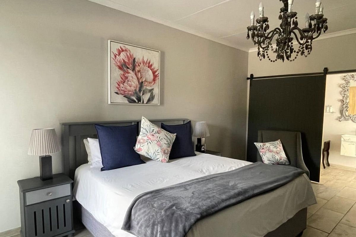 A well-maintained bedroom featuring neutral wall tones, tiled flooring, a sliding barn door, and an elegant decorative chandelier.