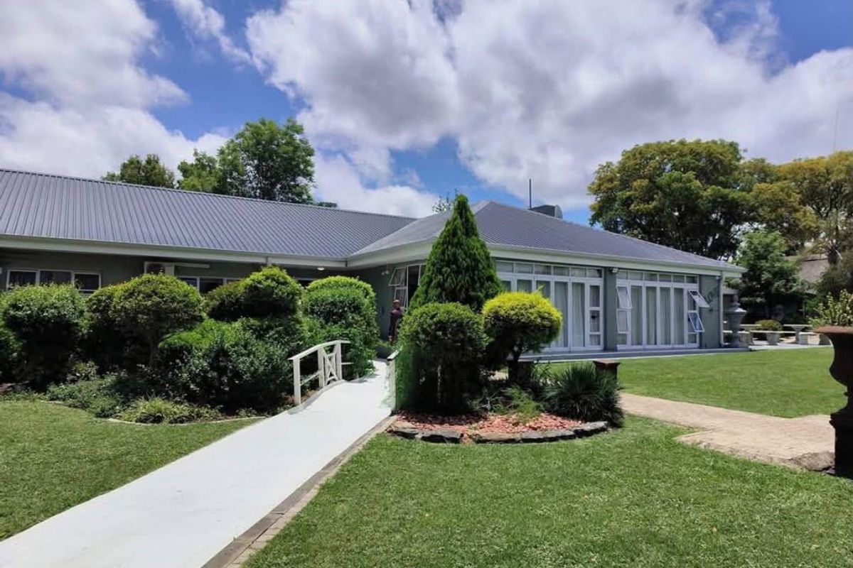 A well-maintained rear exterior view of the farm property featuring a metal roof, expansive folding glass doors, and a manicured garden with paved pathways.
