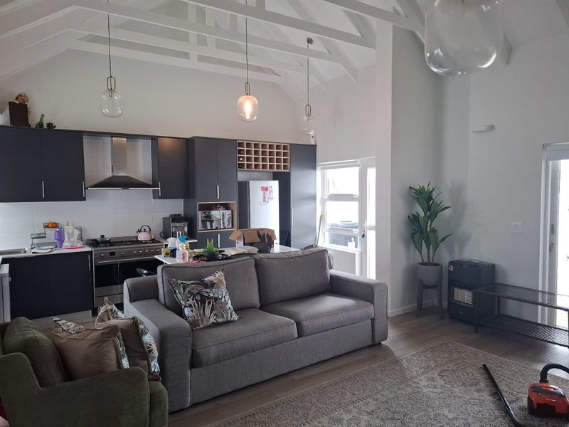 Spacious open-plan living area featuring a modern kitchen with dark cabinetry, vaulted ceilings with exposed rafters, and seamless flow to the lounge space.
