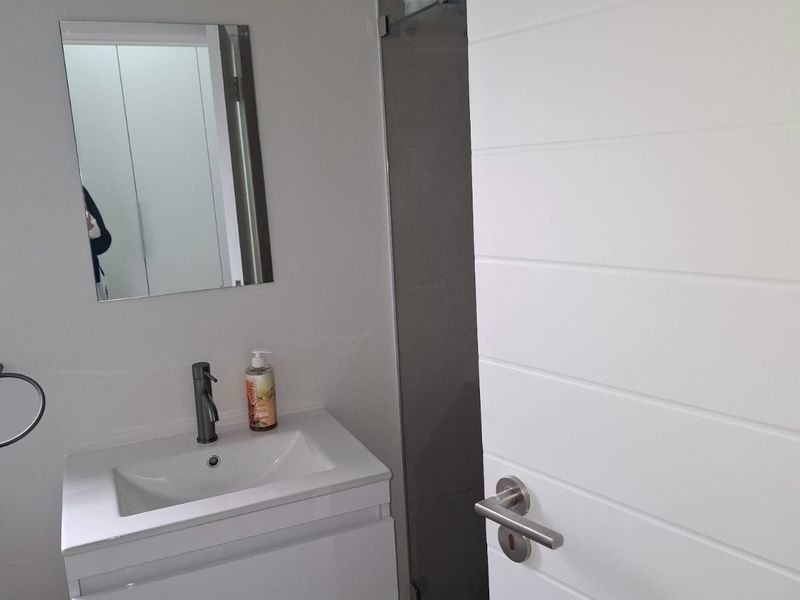 A modern bathroom featuring a white vanity cabinet with a basin, a wall-mounted mirror, and a glass shower enclosure.