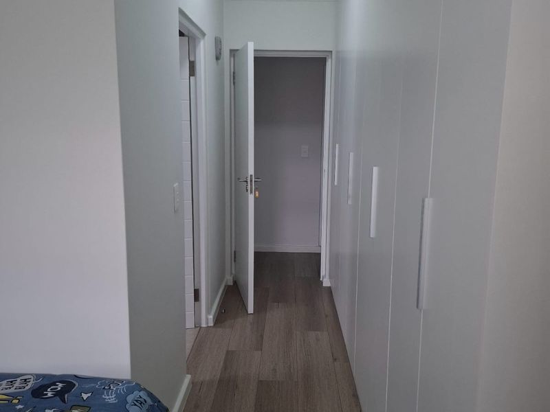 A clean, modern hallway featuring extensive built-in floor-to-ceiling cupboards and durable wood-look laminate flooring.