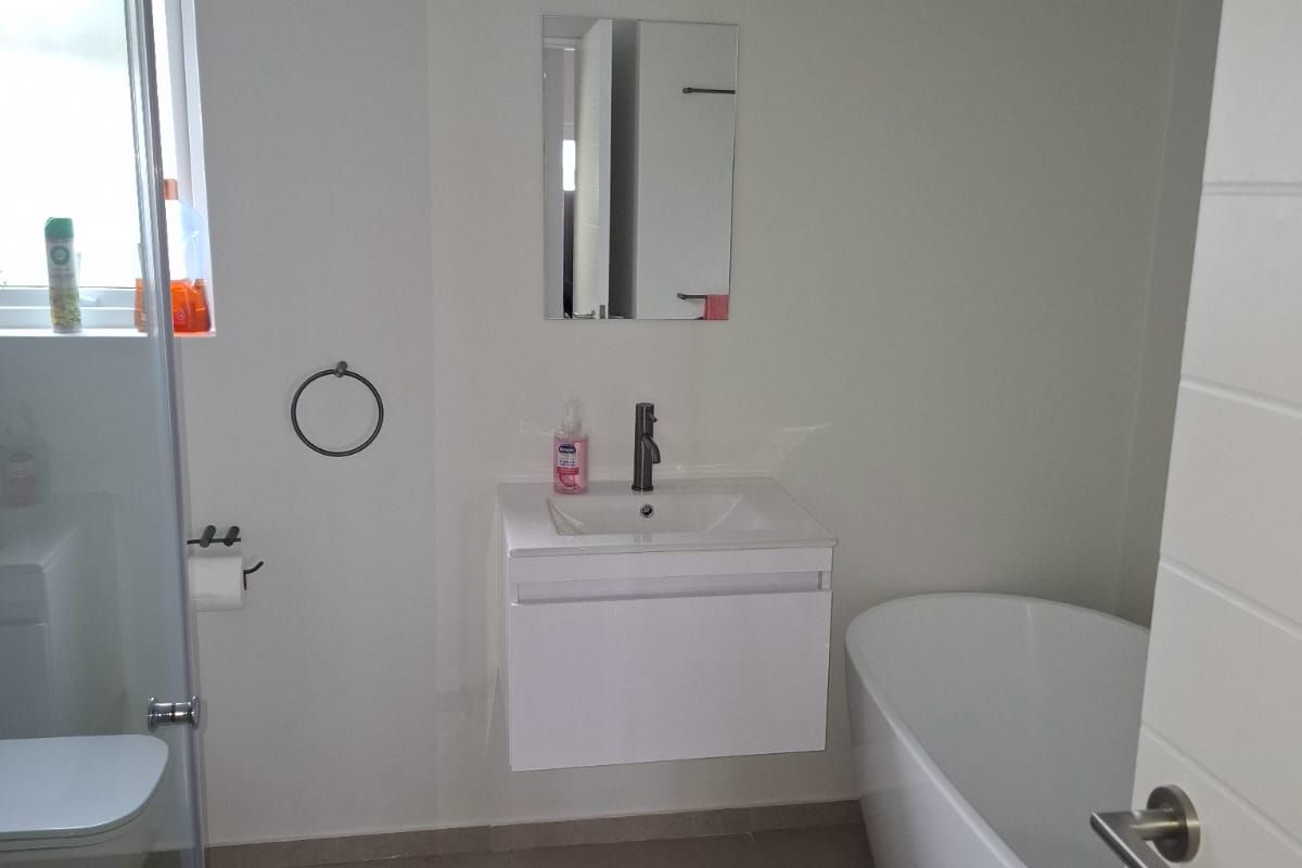 A modern bathroom featuring a wall-mounted vanity, a sleek freestanding bathtub, and a glass-enclosed shower area with neutral floor tiling.