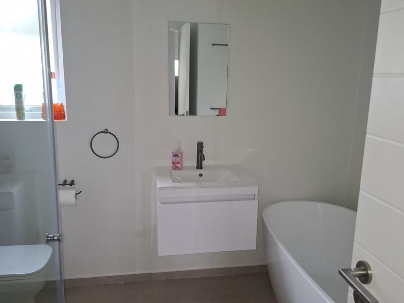 A modern bathroom featuring a wall-mounted vanity, a sleek freestanding bathtub, and a glass-enclosed shower area with neutral floor tiling.