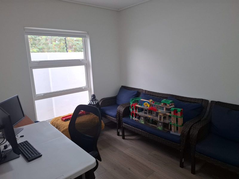 A functional office space featuring laminate flooring and a large window with a roller blind, providing natural light.