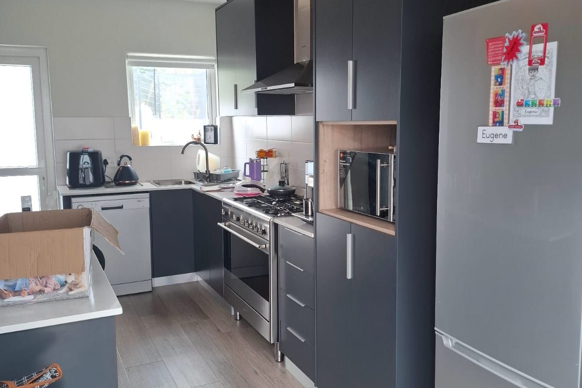Modern kitchen featuring dark cabinetry, gas stove, extractor fan, built-in microwave, wine rack, and light-toned laminate flooring.