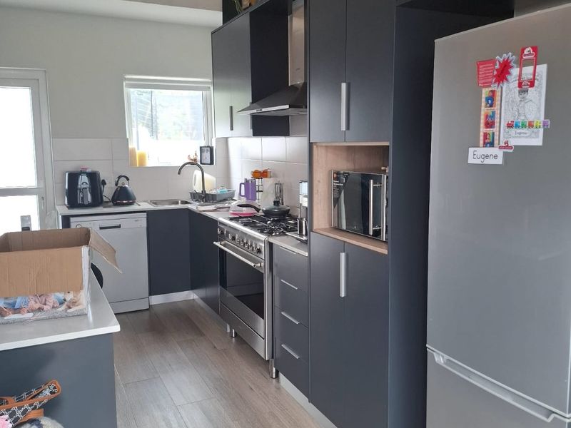 Modern kitchen featuring dark cabinetry, gas stove, extractor fan, built-in microwave, wine rack, and light-toned laminate flooring.