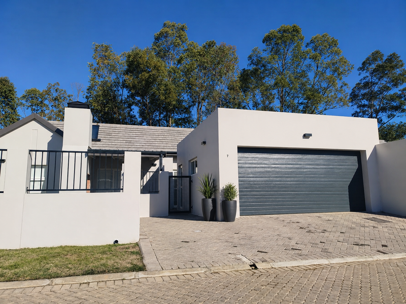 Modern front facade featuring a double garage, paved driveway, and clean architectural lines with a well-maintained boundary wall and fencing.