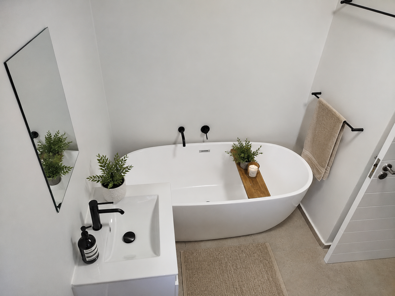 Modern bathroom featuring a sleek freestanding bathtub, wall-mounted basin with black fixtures, and neutral tiled flooring in a clean, contemporary design.