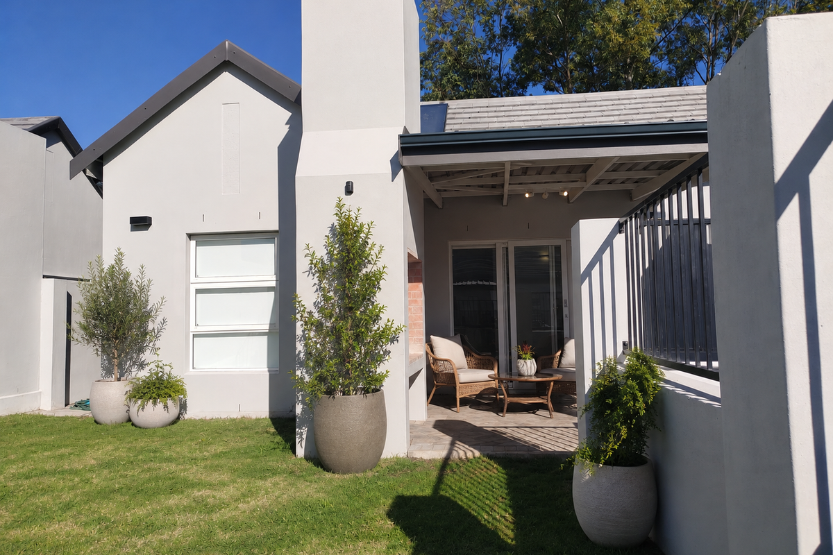 A well-maintained rear exterior featuring a paved patio, built-in braai, and sliding glass doors leading into the home, set against a landscaped garden.