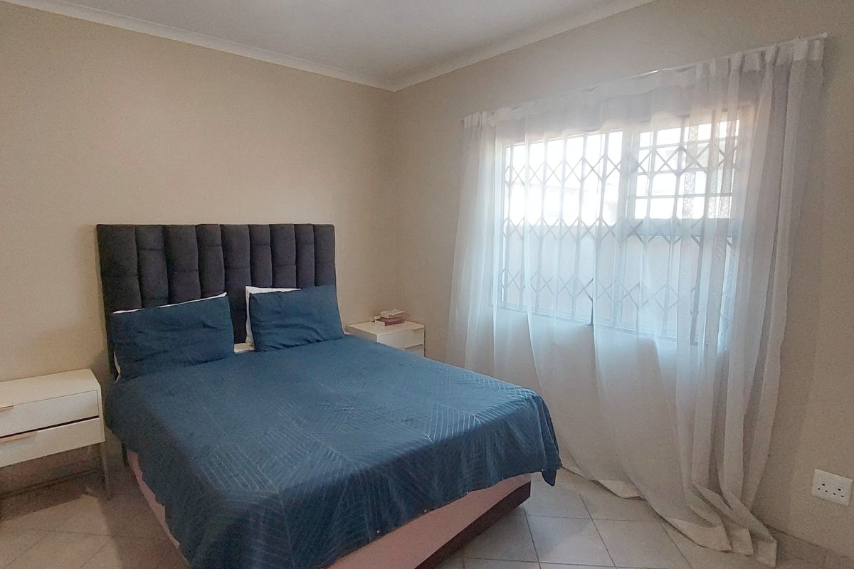 A functional bedroom featuring tiled flooring, a window with a security gate, and neutral wall finishes.