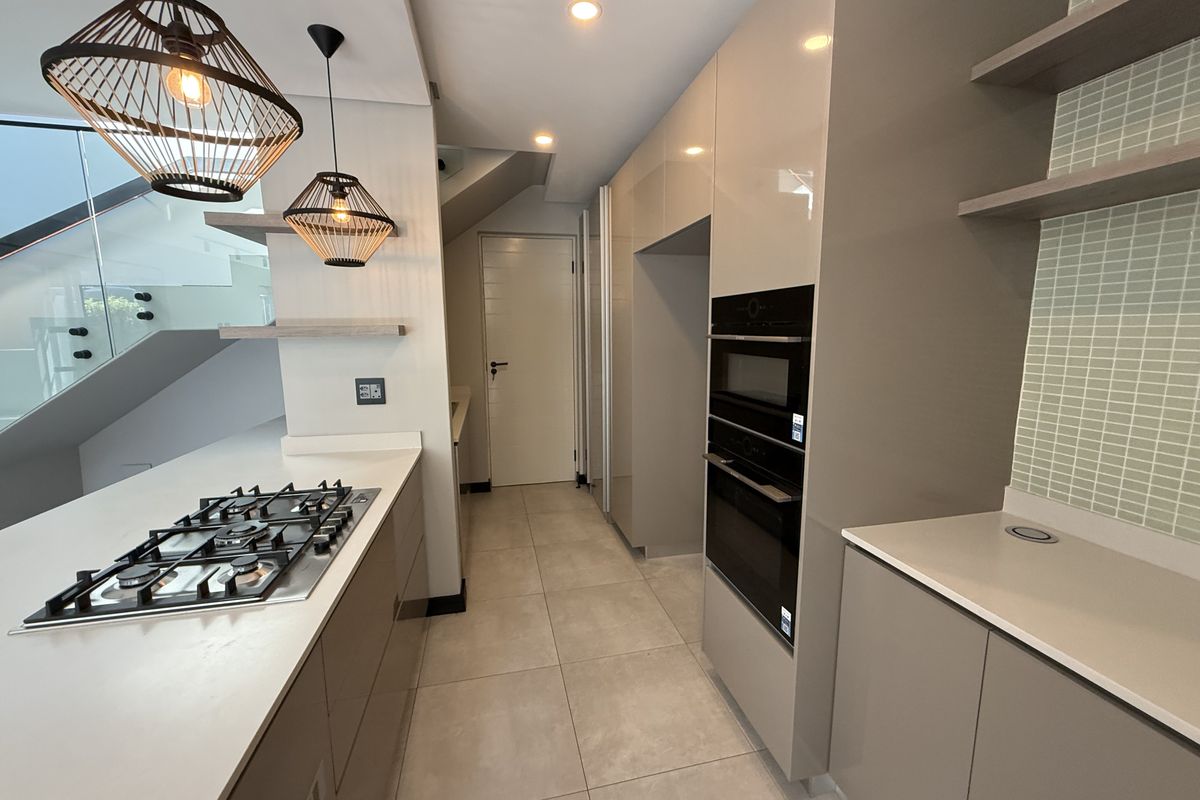 Modern kitchen featuring high-gloss cabinetry, integrated gas hob, built-in oven and microwave, stone countertops, and stylish pendant lighting.