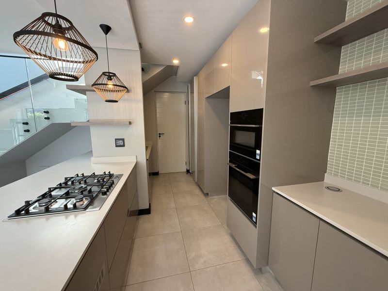 Modern kitchen featuring high-gloss cabinetry, integrated gas hob, built-in oven and microwave, stone countertops, and stylish pendant lighting.