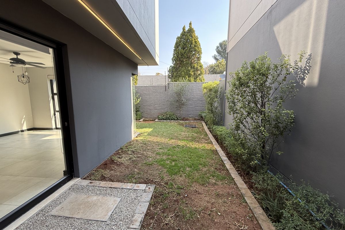 A private rear garden area featuring a paved walkway, boundary walls, and direct access to the interior living space via a large sliding glass door.