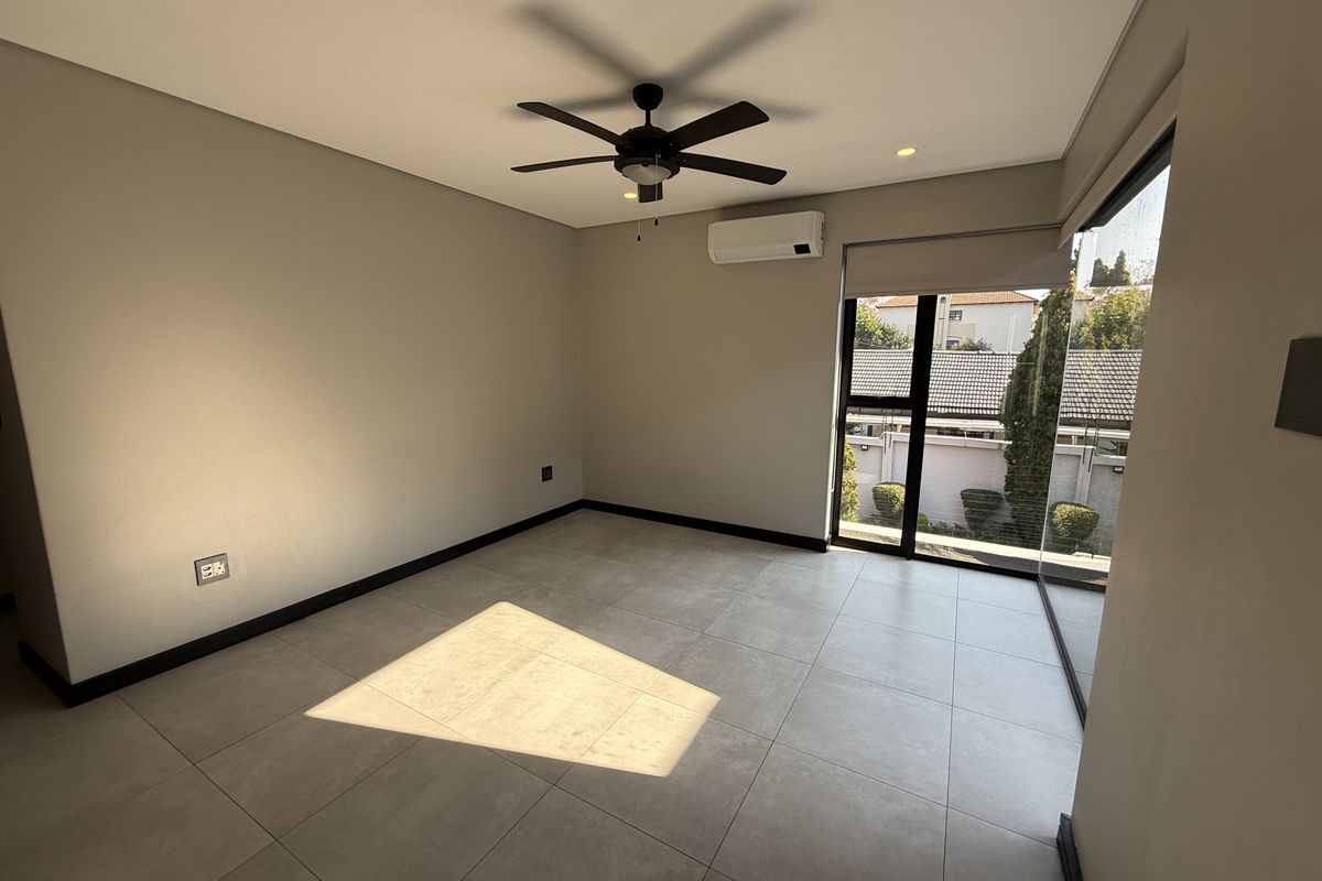 A bright, empty bedroom featuring modern tiled flooring, a ceiling fan, split-system air conditioning, and large glass doors providing natural light.