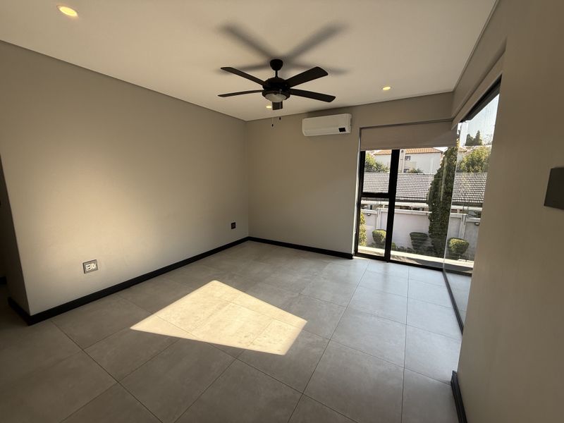 A bright, empty bedroom featuring modern tiled flooring, a ceiling fan, split-system air conditioning, and large glass doors providing natural light.