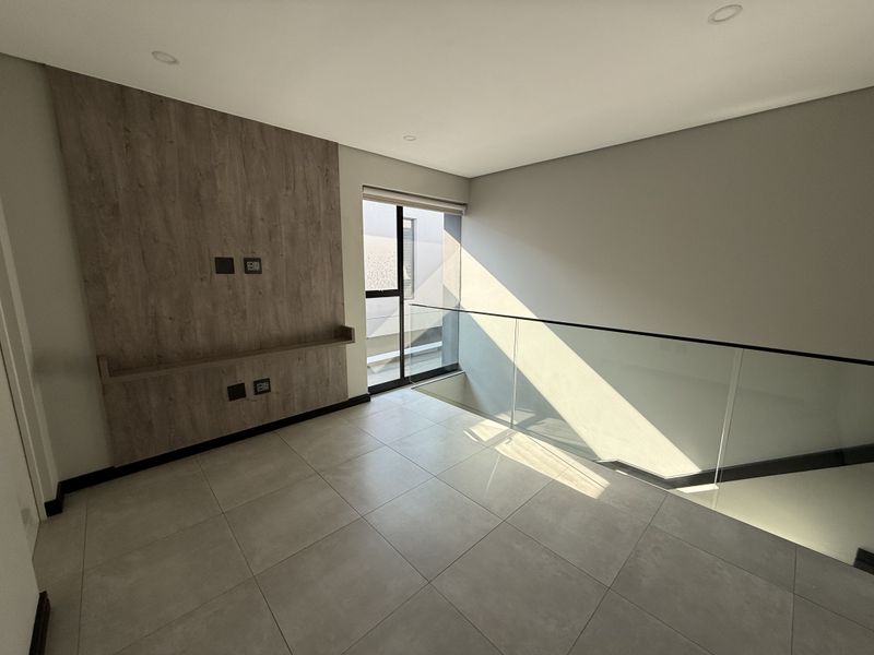 A bright, modern landing or living area featuring a wood-look feature wall, sleek glass balustrade, and neutral floor tiles.