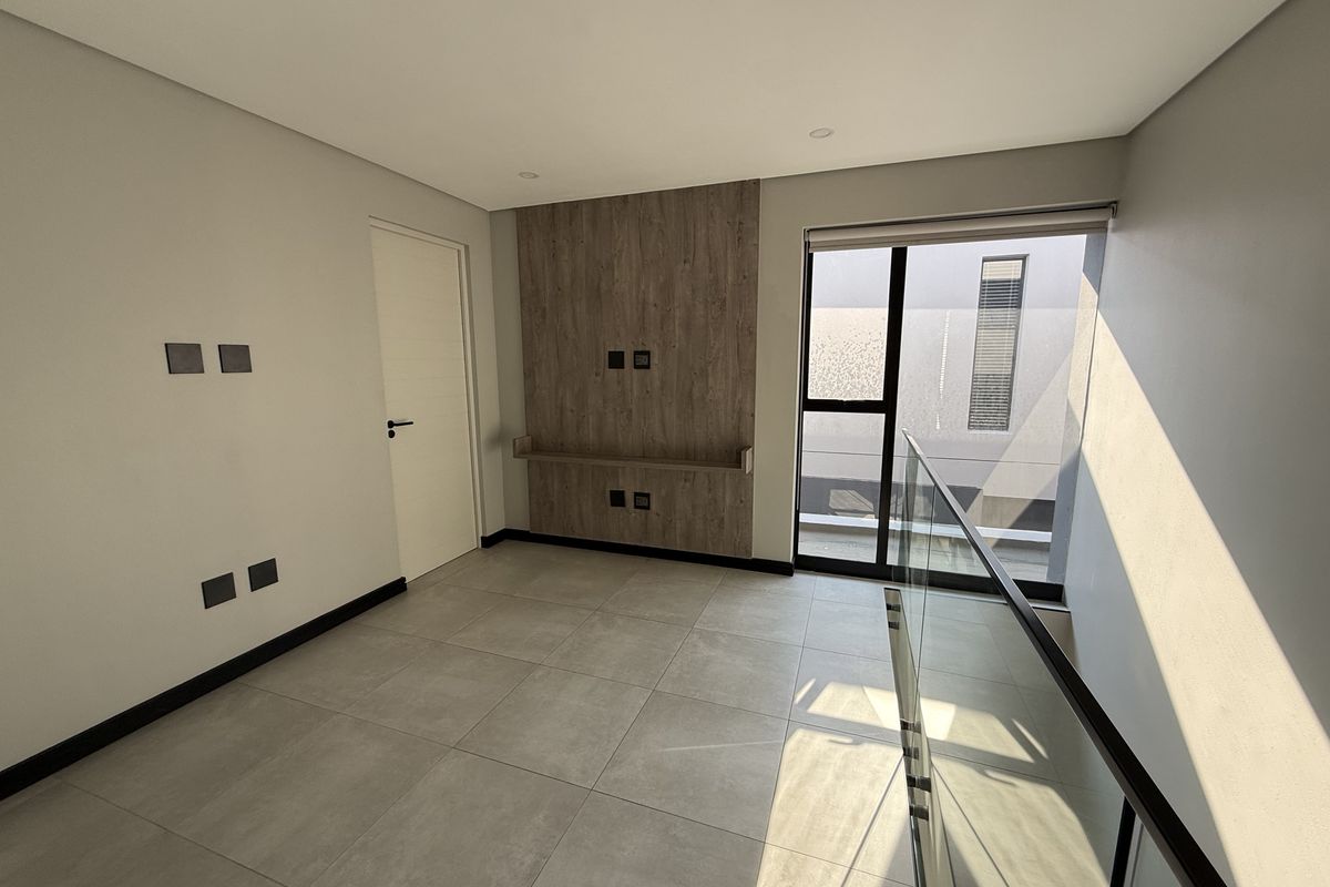 A bright, modern, and empty living area featuring large format floor tiles, a wood-look feature wall with a built-in shelf, and a glass balustrade.