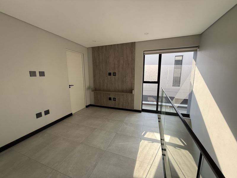 A bright, modern, and empty living area featuring large format floor tiles, a wood-look feature wall with a built-in shelf, and a glass balustrade.