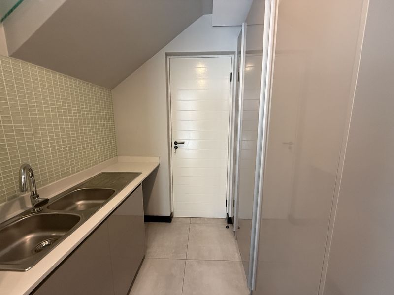 A clean and modern scullery featuring built-in cabinetry, a double stainless steel sink with mixer tap, and neutral tiled finishes.