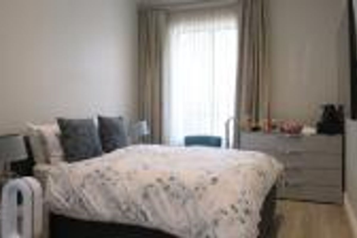 A cozy bedroom featuring neutral walls, laminate flooring, and large windows with curtains, providing a comfortable and well-lit living space.