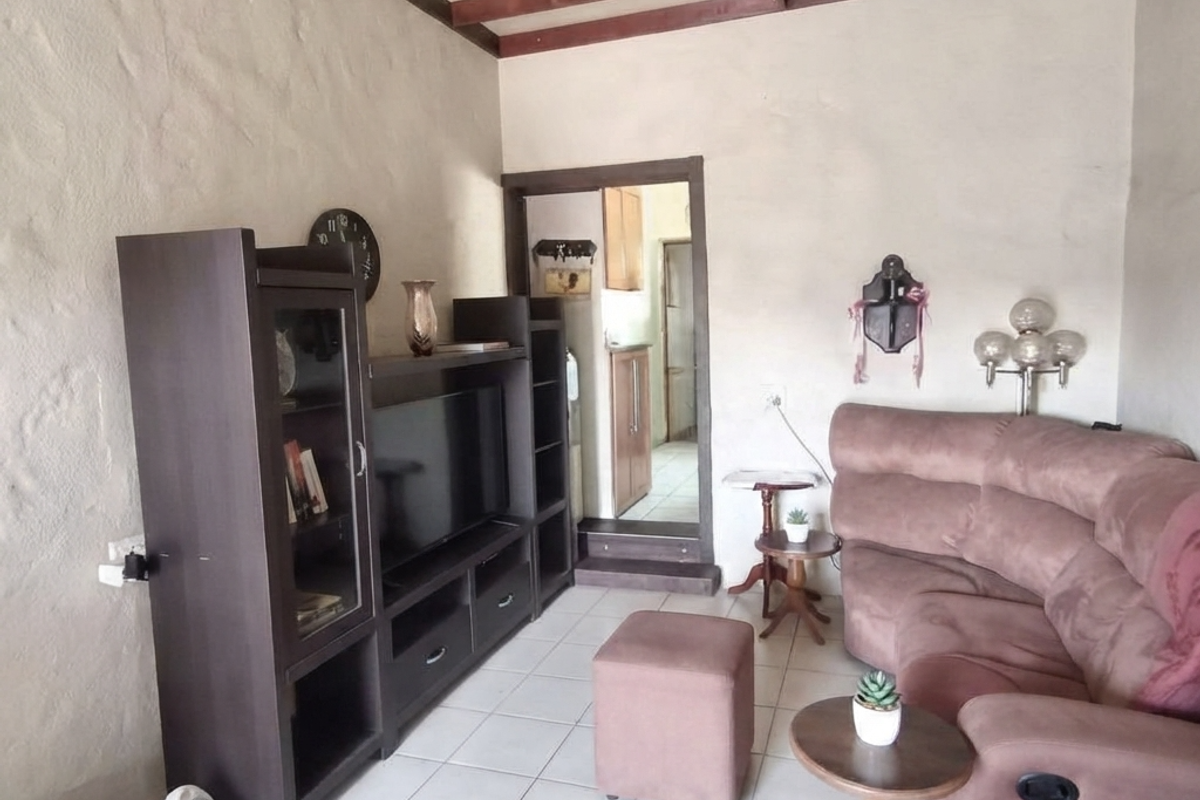 Living room featuring exposed timber ceiling beams, textured walls, and ceramic floor tiles, with an adjacent doorway leading to a secondary space.