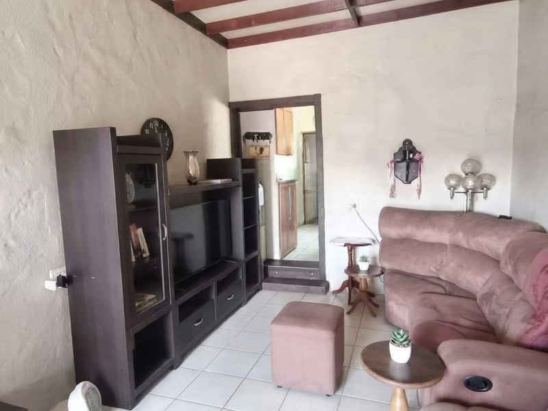 Living room featuring exposed timber ceiling beams, textured walls, and ceramic floor tiles, with an adjacent doorway leading to a secondary space.