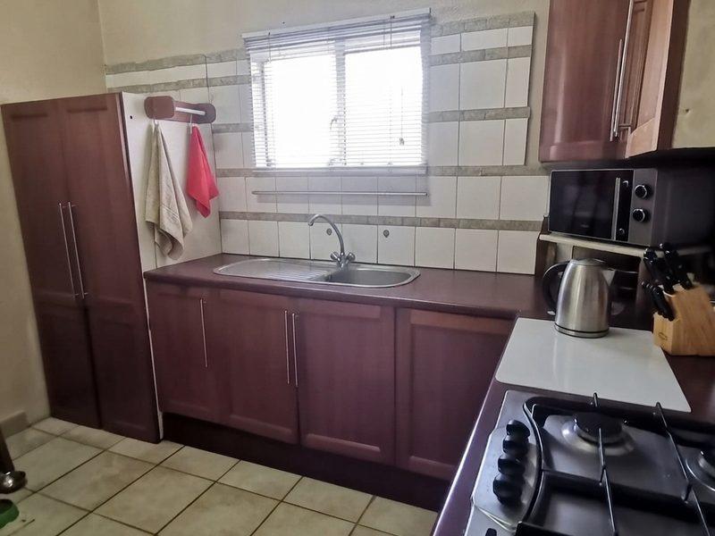 A functional kitchen featuring dark wood-toned cabinetry, a stainless steel sink, tiled splashbacks, and a built-in gas hob with integrated microwave.