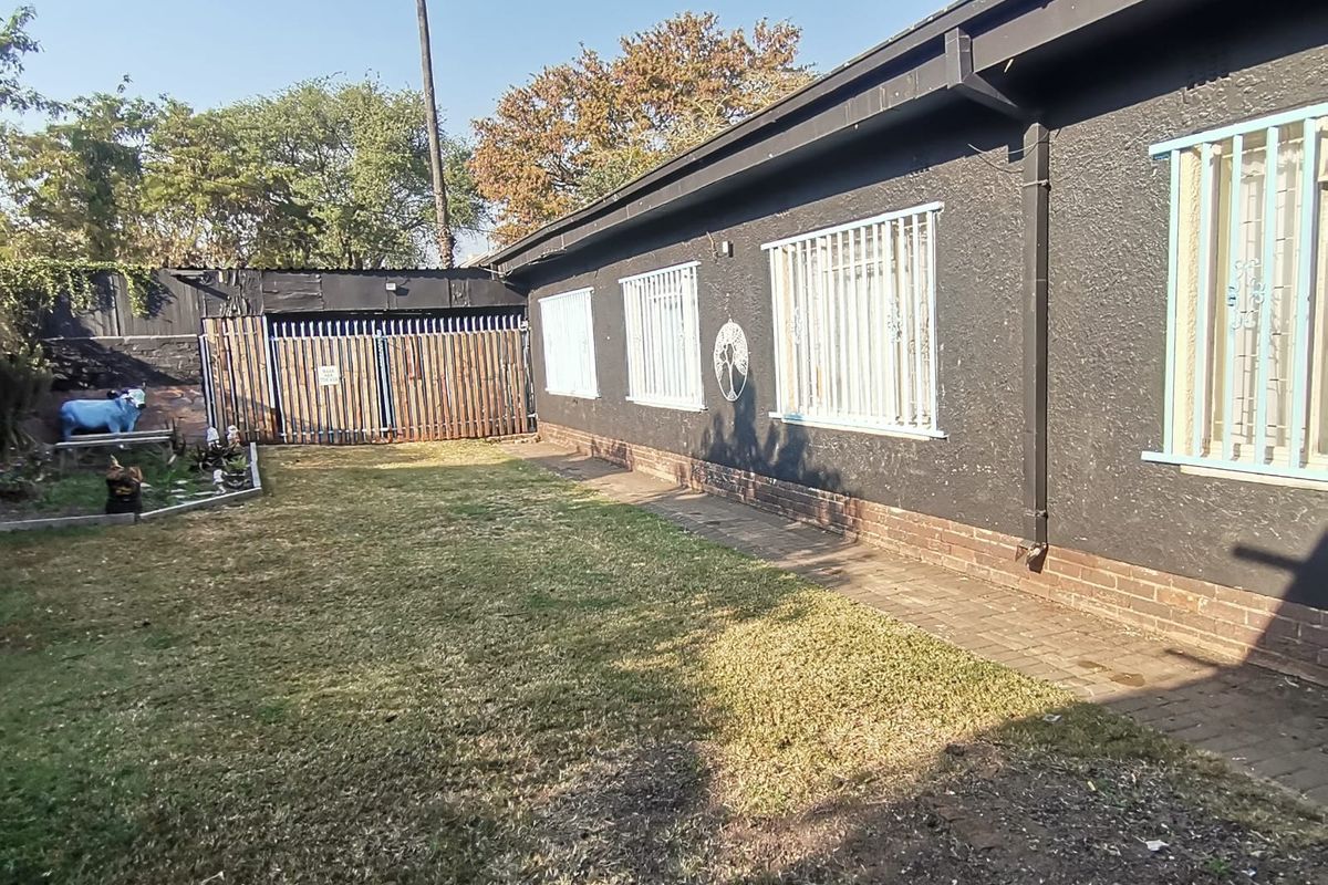 Rear exterior view of the property featuring a lawn area, paved walkway, and security bars on the windows.