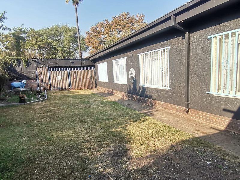 Rear exterior view of the property featuring a lawn area, paved walkway, and security bars on the windows.