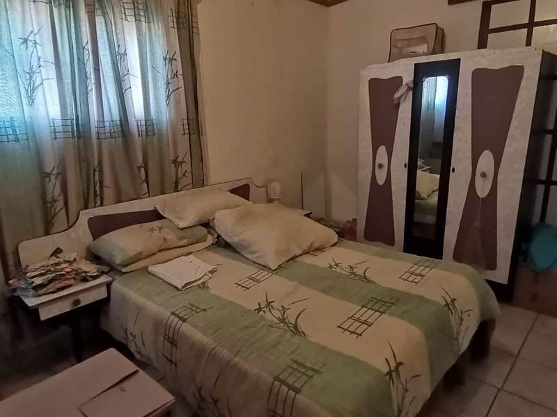 A bedroom featuring tiled flooring and an exposed beam ceiling, currently requiring cosmetic updates to improve its overall aesthetic and condition.