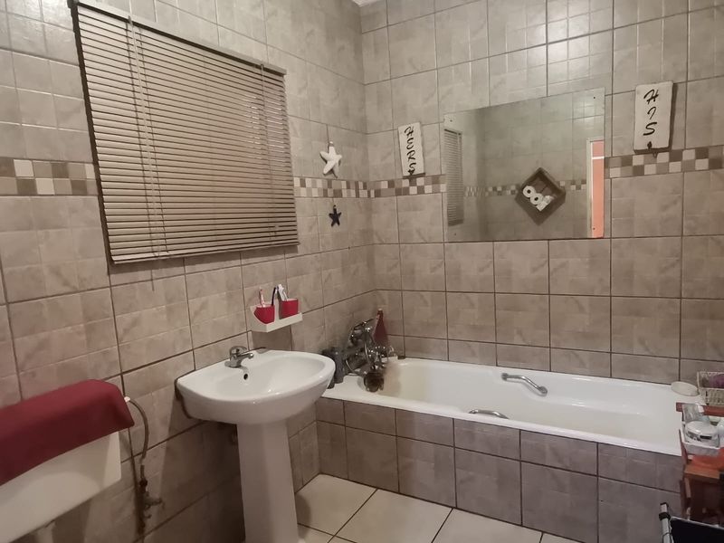 A functional bathroom featuring a pedestal basin, built-in bathtub, and neutral wall and floor tiling throughout.