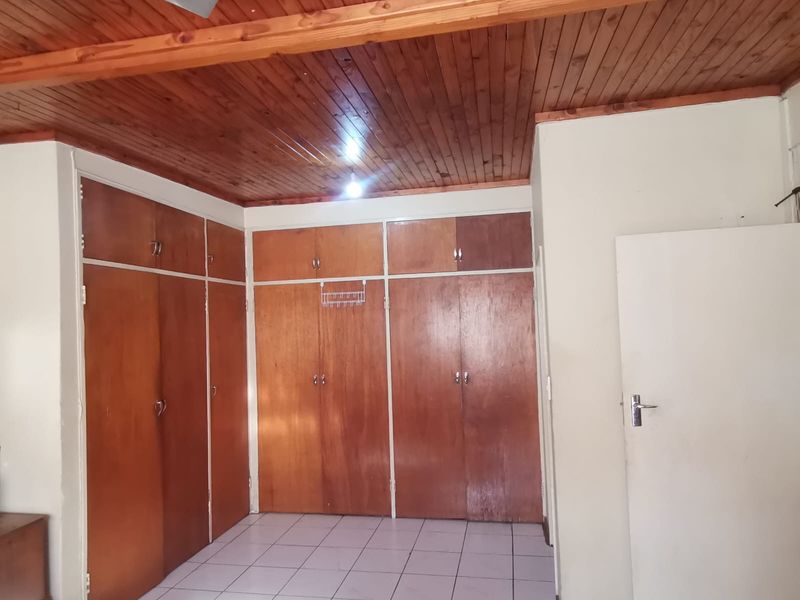 A bedroom featuring extensive built-in wooden cupboards, a timber-clad ceiling with a ceiling fan, and neutral floor tiles.